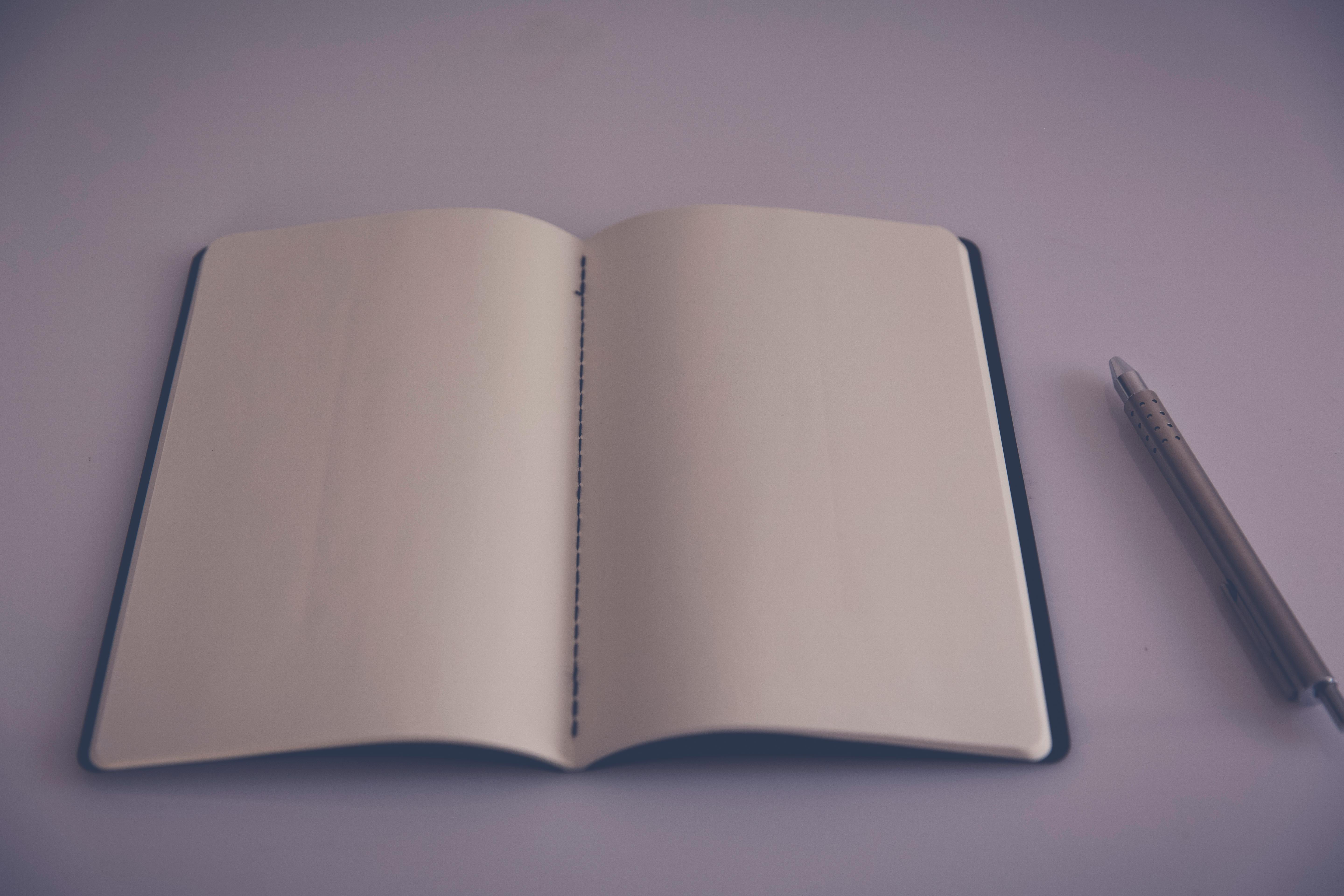 A clean, empty desk with a single pen sitting next to a white notebook